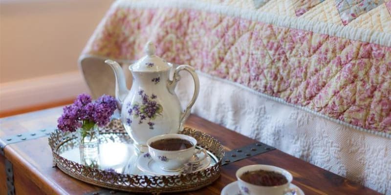 White with violet flowers Tea service on a tray placed on cedar trunk at base of bed