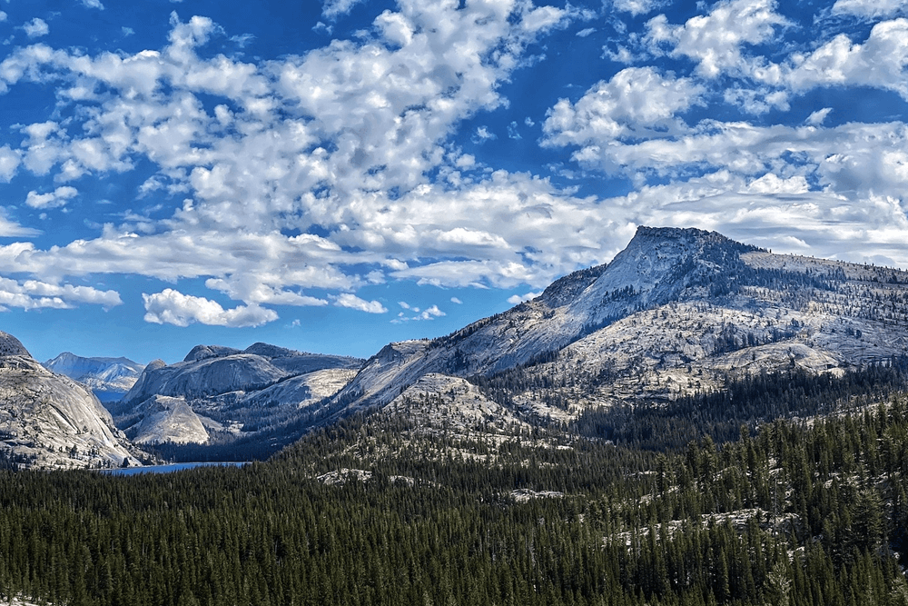 The image showcases a rugged mountain range with towering peaks, dramatic clouds, and a foreground of rocky terrain.