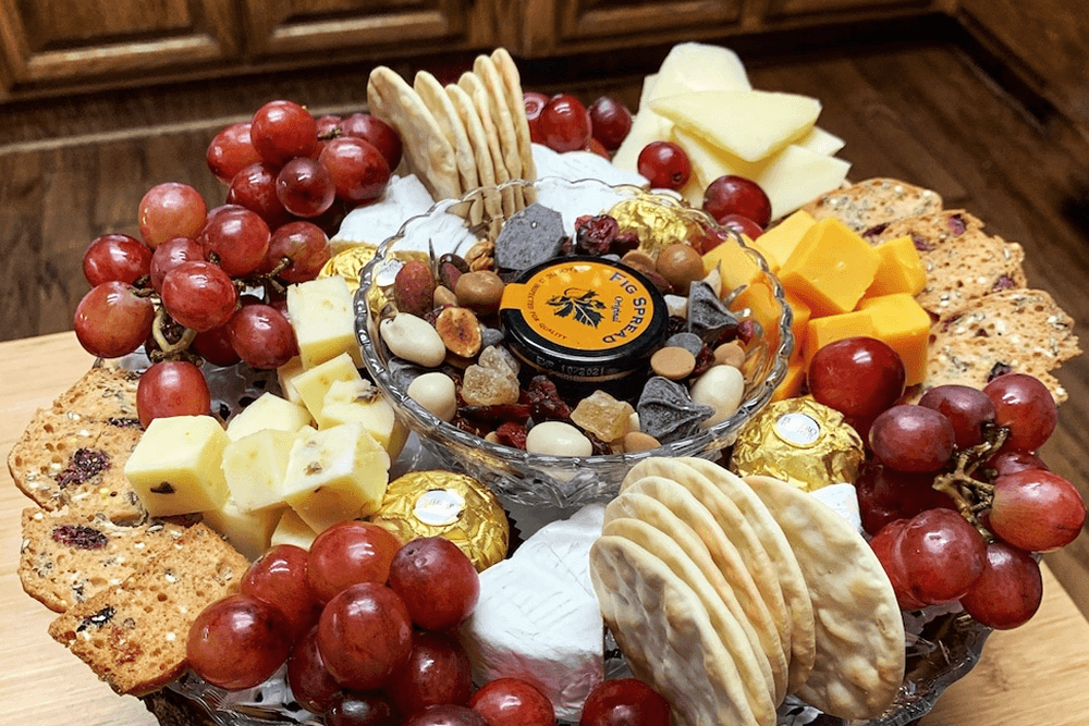 A beautifully arranged cheese board with a variety of cheeses, fruits, crackers, nuts, and chocolates.