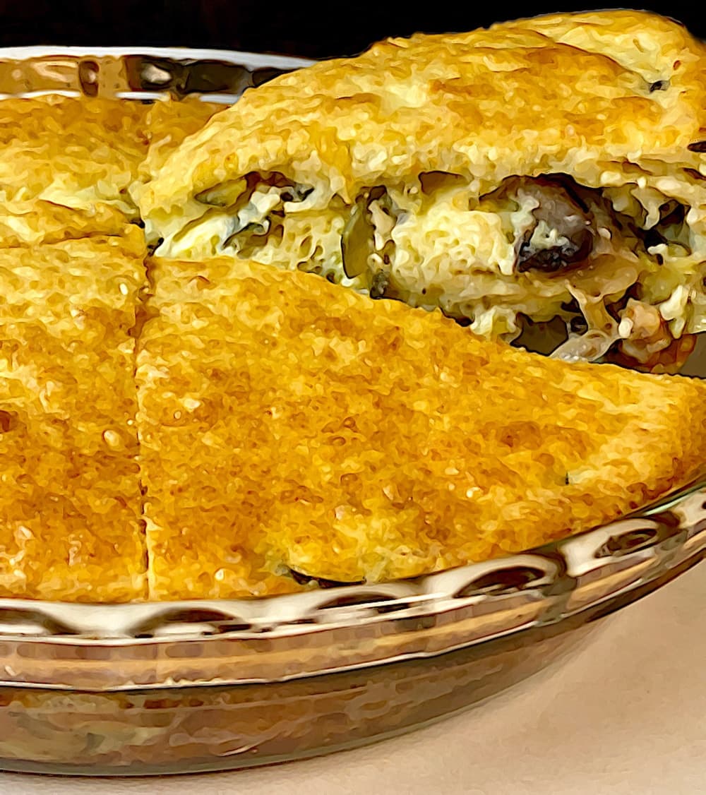 A delicious-looking baked dish with a golden crust, filled with a creamy filling that appears to contain cheese, mushrooms, and possibly chicken. A slice has been cut, revealing the layers of the filling.